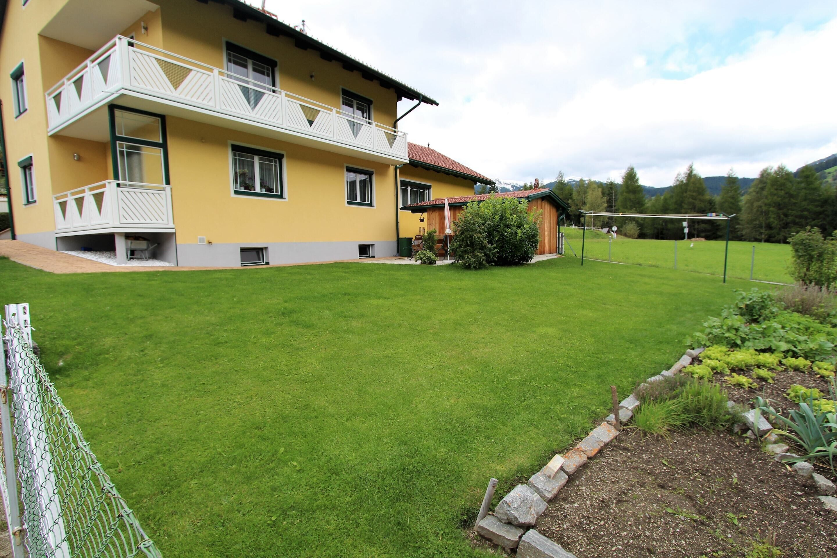 Ein zweistöckiges Gebäude mit Balkon, gepflegtem Rasen und einem Gemüsegarten.