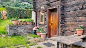 A rustic wooden house with a stone wall and a wooden door. There are potted plants and a small wooden table outside. - Holiday Home in Tyrol Near Ski Slopes (Matrei in Osttirol)