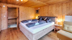 A wooden cabin bedroom with a bed, a nightstand, a chair, and a wooden door leading to a balcony. - Holiday Home in Tyrol Near Ski Slopes (Matrei in Osttirol)