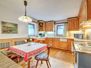 A cozy kitchen with wooden cabinets, a dining table with a red and white tablecloth, and a vase with flowers. - Holiday Home in Tyrol Near Ski Slopes (Matrei in Osttirol)