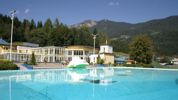 Une piscine avec un bateau, entourée d’immeubles et de montagnes.