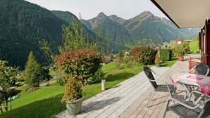 Un patio con mobiliario exterior, vistas a un paisaje montañoso y una pequeña zona ajardinada con plantas en macetas.