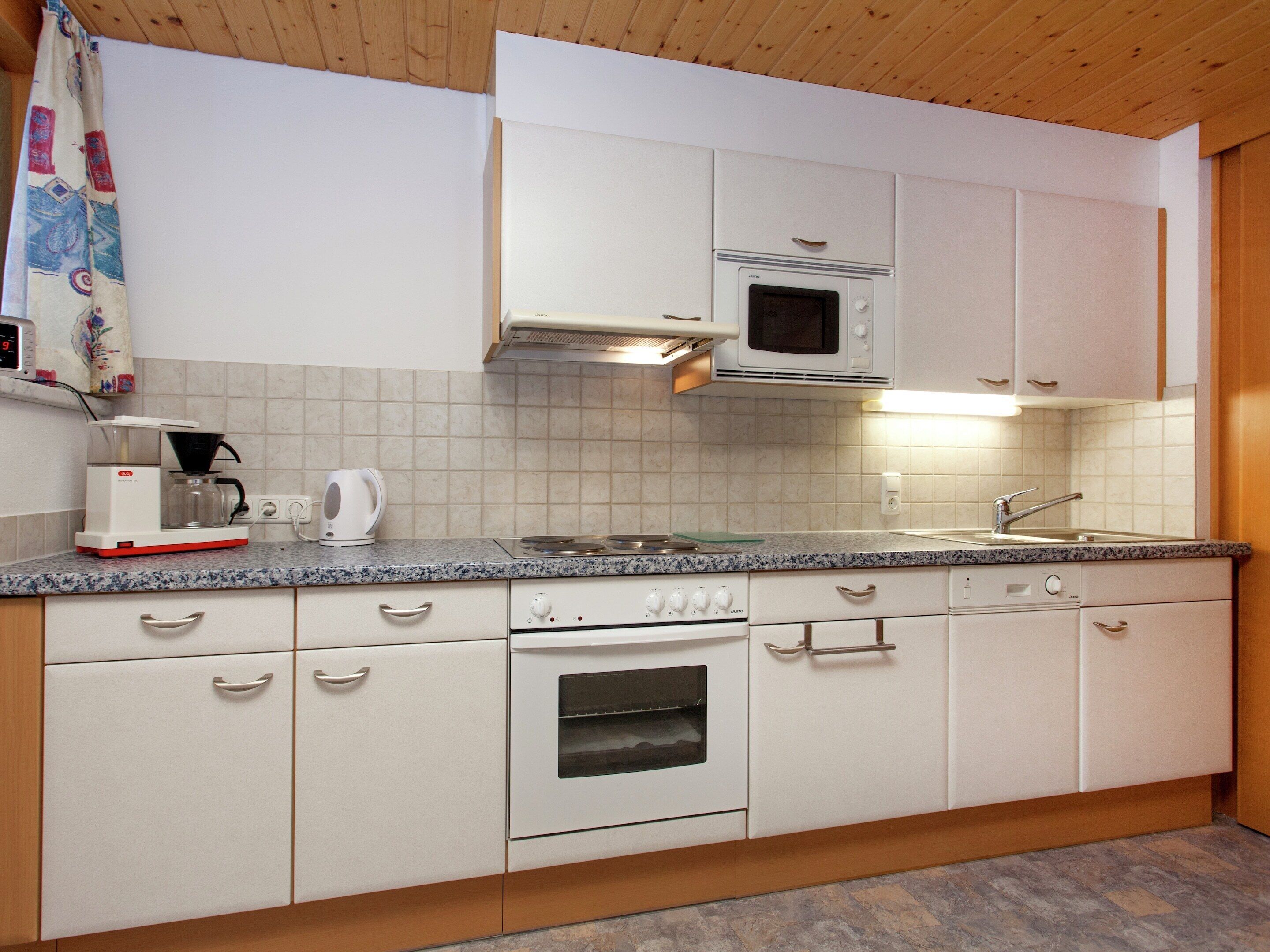 A kitchen with white cabinets, a microwave, a stove, a coffee maker, and a sink.