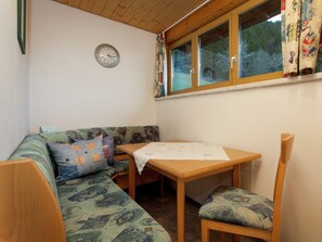 Une pièce d’angle avec un banc en bois, une petite table, une horloge au mur et une fenêtre avec des rideaux.