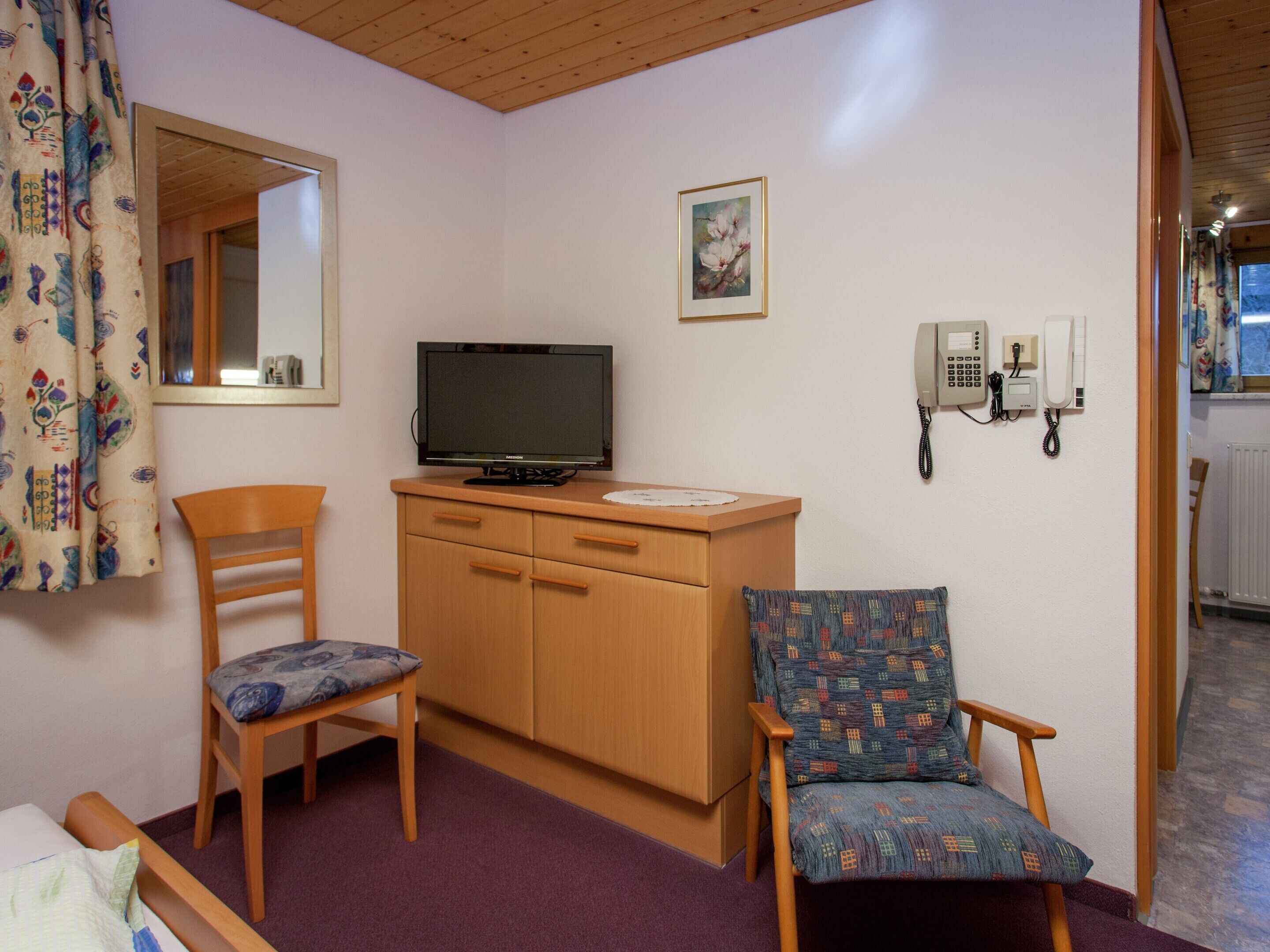 Une chambre avec un lit, un bureau en bois, une télévision, un téléphone et une chaise à motifs.