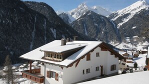 Una casa en la montaña cubierta de nieve, con balcón y vistas de las montañas circundantes.
