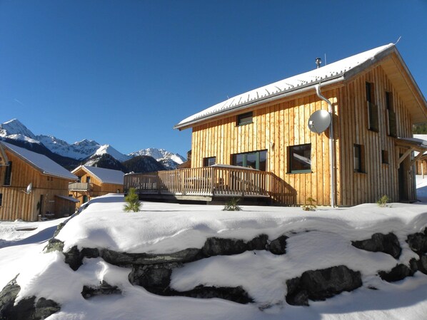 Eine Holzhütte mit einem Balkon vor einer verschneiten Bergkulisse.