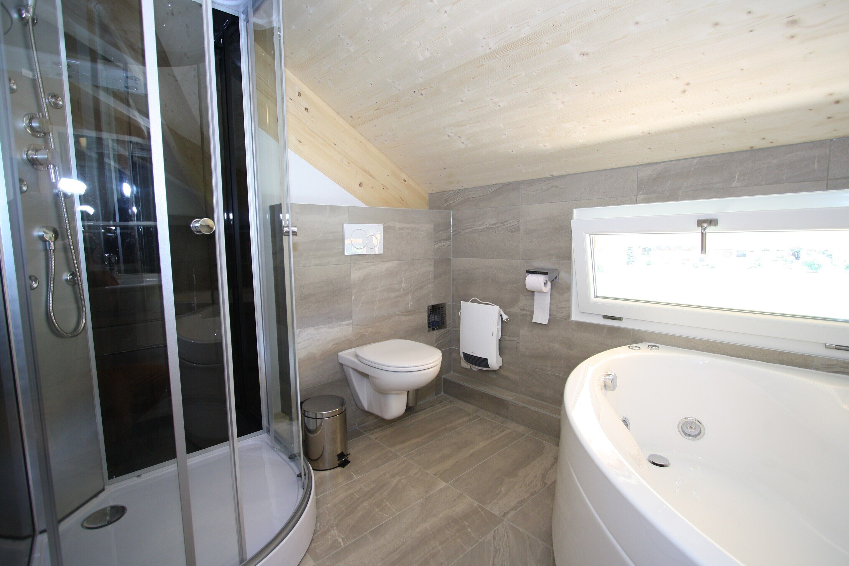Ein modernes Badezimmer mit Duschkabine aus Glas, Toilette und einer großen Badewanne.