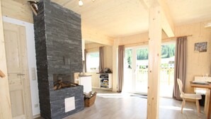 A spacious living area with a stone fireplace, wooden flooring, and a view of the outdoors. - Wooden Chalet in Hohentauern With Sauna (Hohentauern)