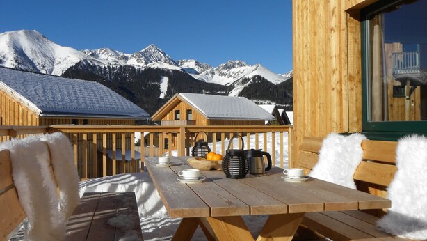 A wooden deck with a table and chairs, overlooking snow-covered mountains. - Wooden Chalet in Hohentauern With Sauna (Hohentauern)