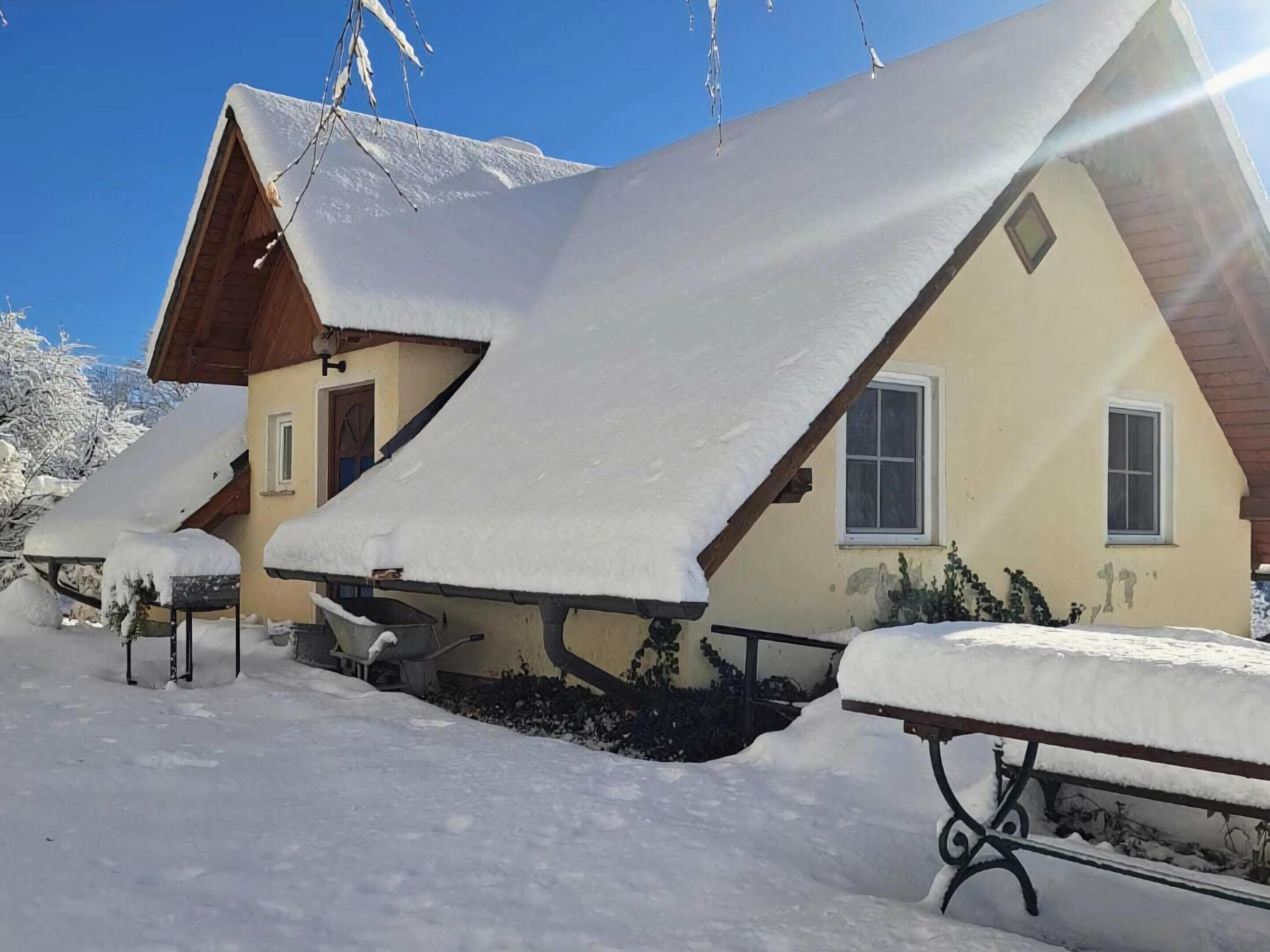 Un chalé con techo inclinado cubierto de nieve, una escalera de madera y un pequeño ventanal.