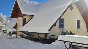 Un chalé con techo inclinado cubierto de nieve, una escalera de madera y un pequeño ventanal.
