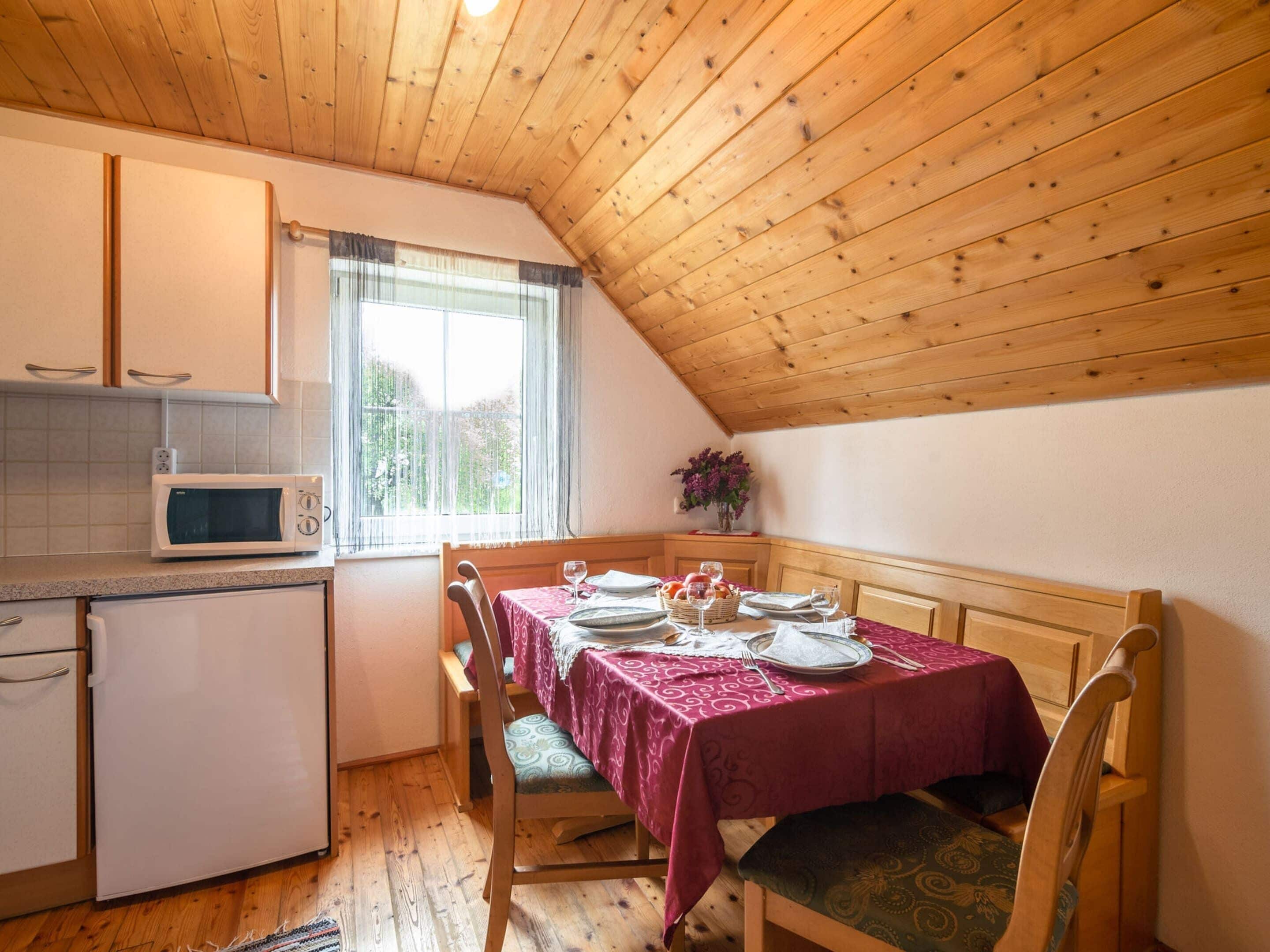 A cozy kitchen with wooden ceiling, a dining table set for two, and a microwave.