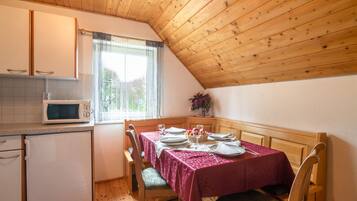 A cozy kitchen with wooden ceiling, a dining table set for two, and a microwave.