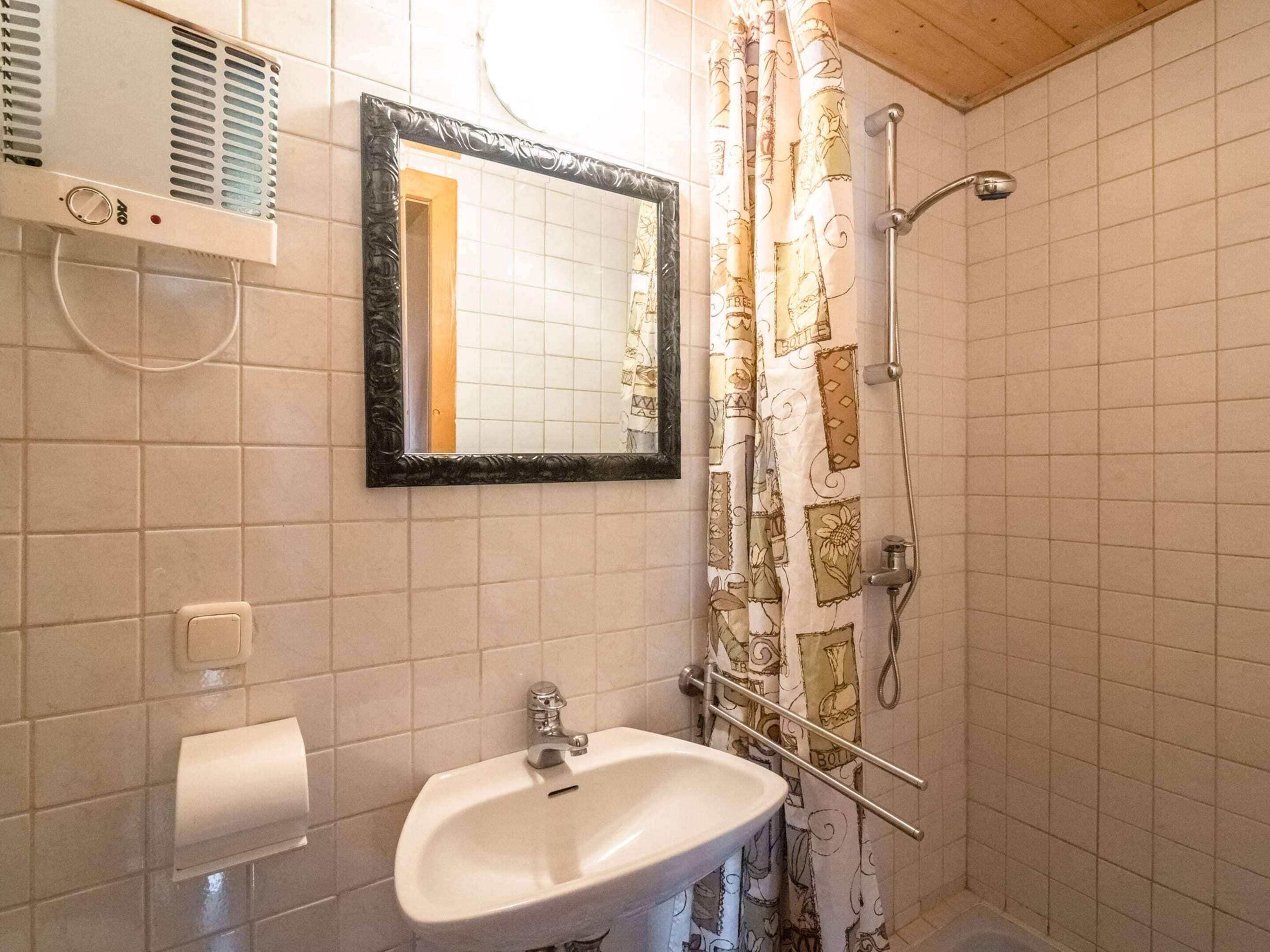 A bathroom with a white sink, a mirror, a shower with a curtain, and a towel dispenser.