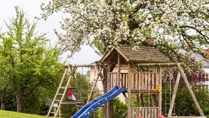 A wooden play structure with a slide and swings, surrounded by grass and trees. - Chalet in Sankt Andra Near Koralpe Ski Area (Sankt Andra)