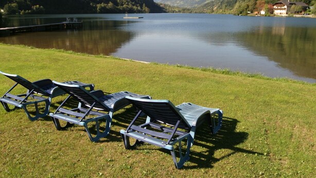 Une vue sur le lac, avec des chaises longues sur la pelouse, un quai et un bâtiment en arrière-plan.