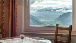 Une pièce avec une table et une chaise, une fenêtre donnant sur des montagnes et une vallée, et une lampe sur la table.