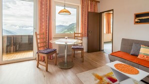 Un salon chaleureux avec un canapé, une table à manger et des chaises, et une vue sur les montagnes grâce à de grandes fenêtres.