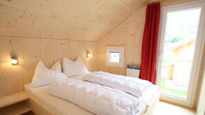 A wooden cabin bedroom with a bed, two wall-mounted lights, a small window, and a red curtain. - Nice Chalet in Hohentauern / Styria With Sauna (Hohentauern)