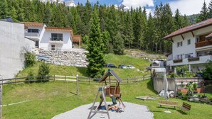 A playground with a swing set and a sandbox in a grassy area with a stone wall and a wooden fence. - Apartment in Strengen Near Ski Bus (Strengen)