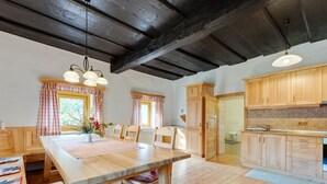 Eine geräumige Küche mit Holzschränken, eine Essecke mit großem Tisch und eine Decke mit freiliegenden Balken.
