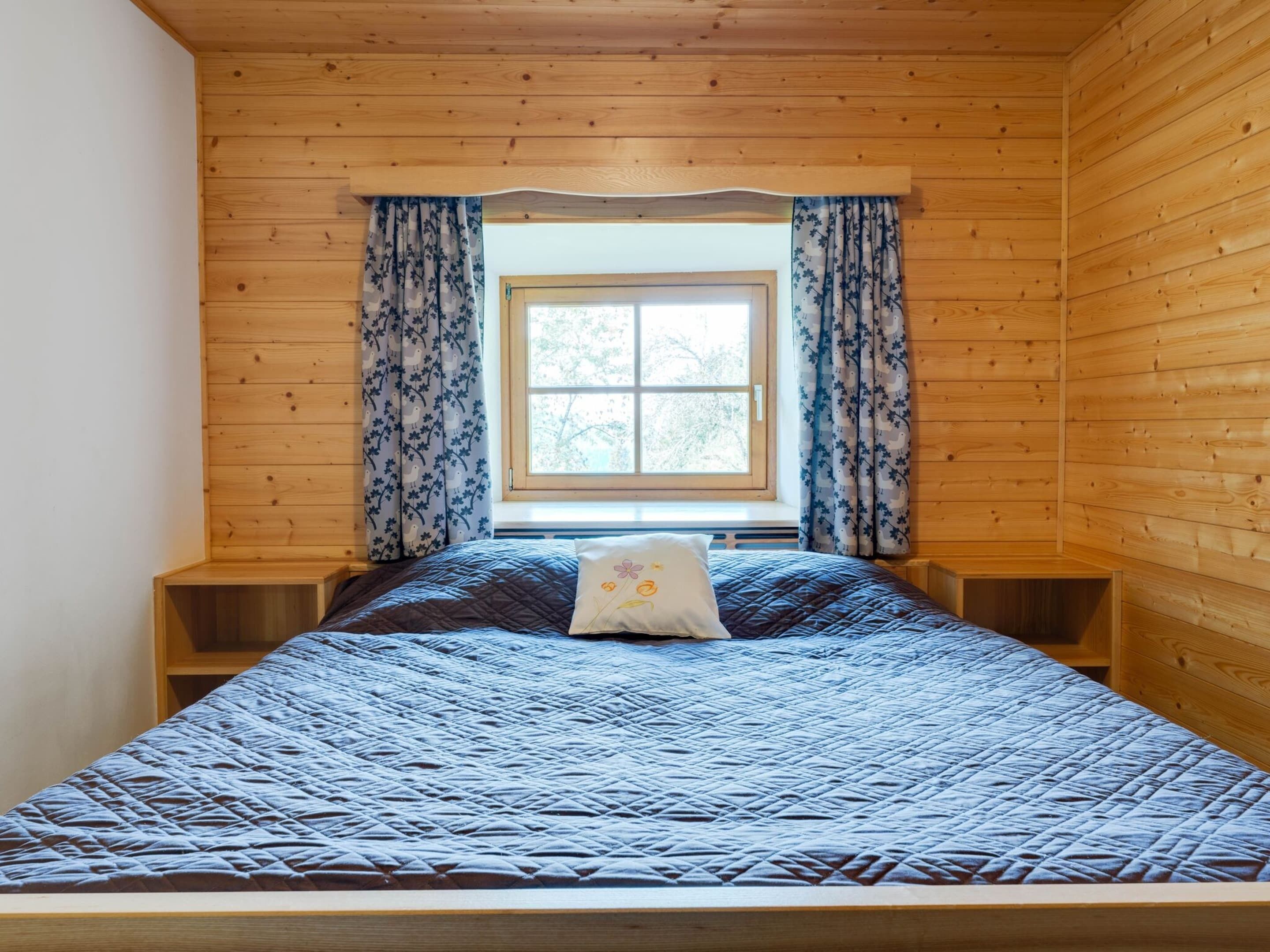 Une chambre à coucher avec un lit, une fenêtre avec des rideaux et des murs en bois.