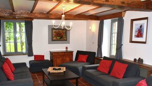 Ein gemütliches Wohnzimmer mit grauen Sofas und roten Kissen, einer Holzkommode und einer Pendelleuchte.