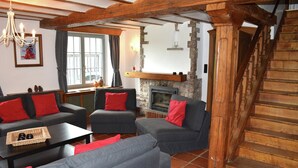 Ein gemütliches Wohnzimmer mit grauen Sofas, roten Kissen, einem Kamin und einer Holztreppe.