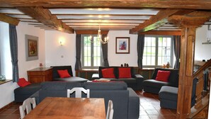 Ein gemütliches Wohnzimmer mit einem Holzesstisch, grauen Sofas mit roten Kissen, einer Chandelier und einer Treppe.