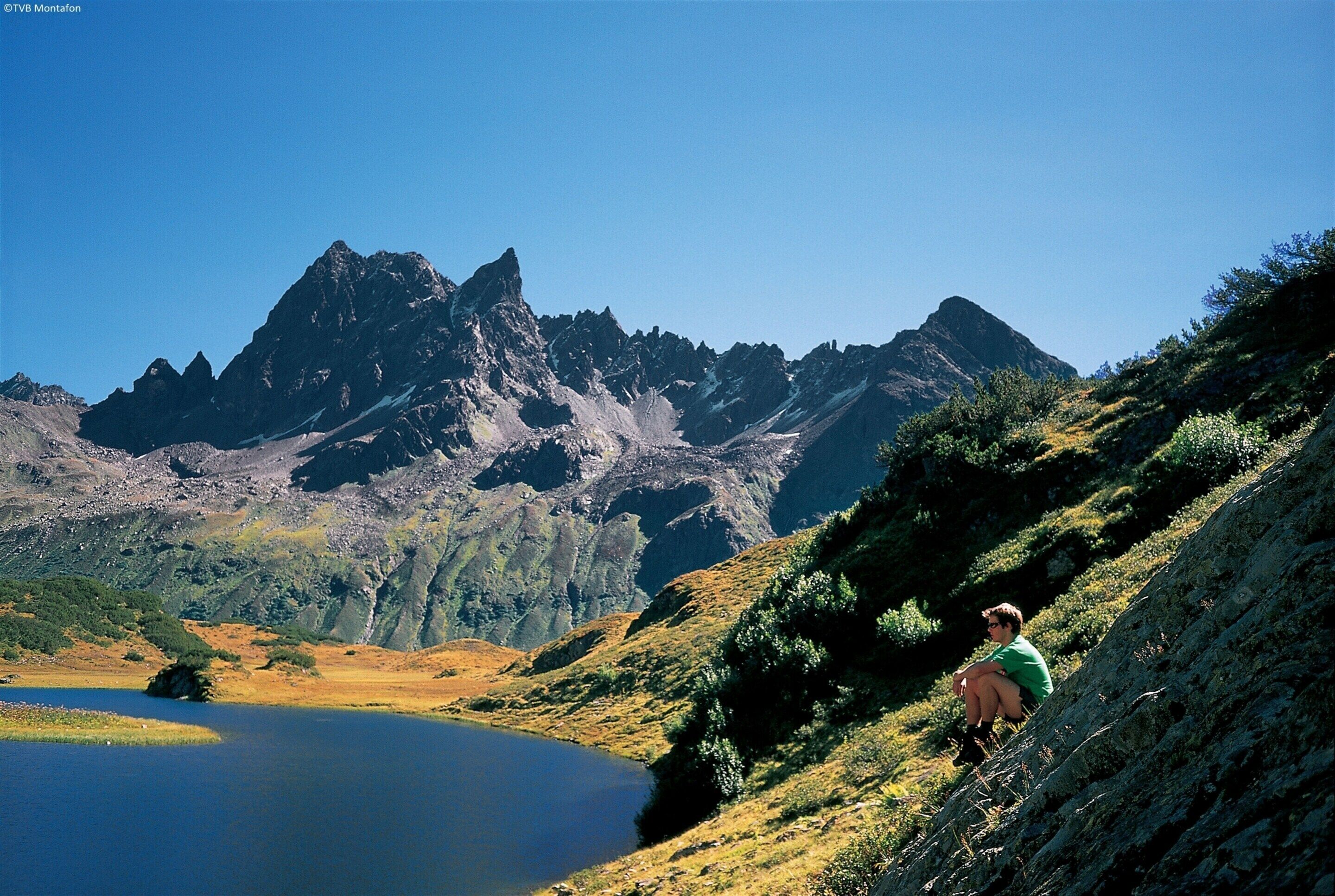 Un paysage montagneux avec un lac et une personne assise sur une colline.