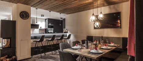 A modern dining area with a wooden ceiling, a kitchen in the background, and a bar seating area.