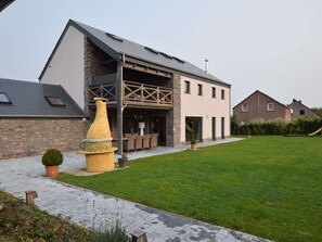 Een modern gebouw met een stenen gevel, een overdekt terras en een verzorgd gazon.