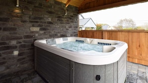Ein Whirlpool in einem überdachten Außenbereich mit Steinwänden und Holzbalken.