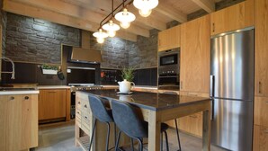 Eine moderne Küche mit einer großen Kochinsel, Edelstahlgeräten, Holzschränken und einer Wand mit Steinverkleidung.