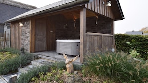 Eine rustikale Holzhütte mit Steinaußenwand, einer Holzterrasse und einem Whirlpool.