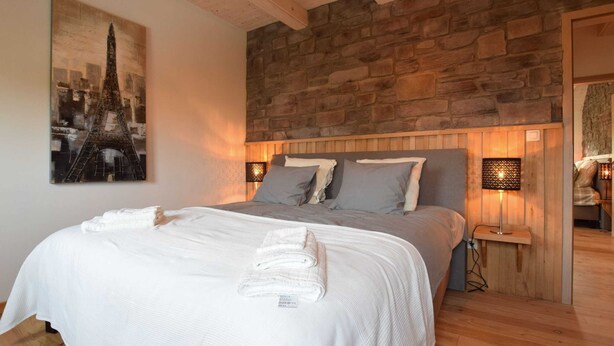 Ein Schlafzimmer mit Steinwand, einem Bett mit grauer Bettwäsche und einem Stadtbildgemälde.