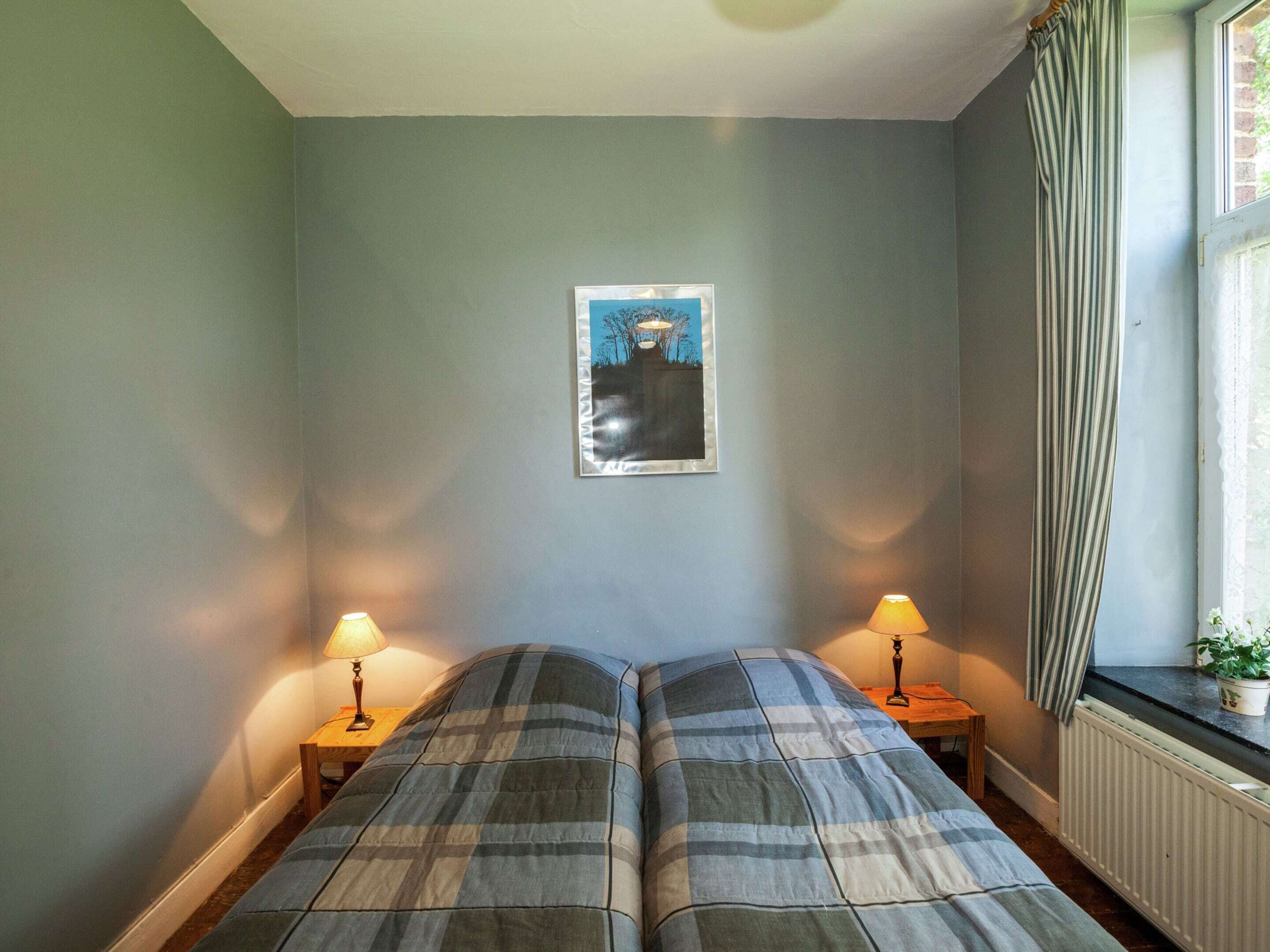 A room with two beds, a framed picture on the wall, and a window with curtains.