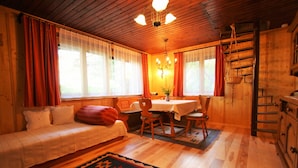 A cozy room with a bed, a dining table, chairs, a chandelier, and a wooden staircase. - Queitly Located Chalet near Resort Center of Nassfeld (Hermagor-Pressegger See)