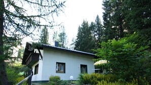 A house with a white exterior, a wooden deck, and a garden with yellow flowers. - Queitly Located Chalet near Resort Center of Nassfeld (Hermagor-Pressegger See)
