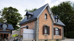 Une maison à deux étages, construite en briques, avec un toit en pente, un garage fermé et une allée gravillonnée.