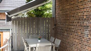 Een terras buiten met een tafel, stoelen, een houten hek en een bakstenen muur.