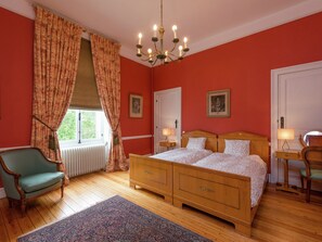 A bedroom with a wooden bed, two bedside tables, a chair, and a window with curtains. - Beautiful Manor House in a Park Near Rochefort (Nassogne)
