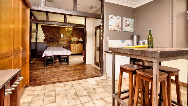 Una cocina con una mesa de madera y taburetes, una pared de piedra y un suelo de baldosas.