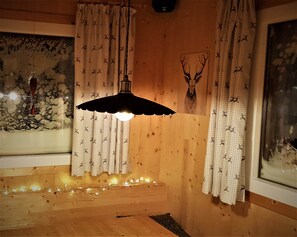 Huone, jossa on puuseinät, ruutukuviolliset verhot, kattotuuletin ja seinällä oleva peuranpään koriste.