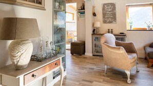 A cozy living room with a wooden floor, a beige armchair, a white cabinet with glass doors, and a chalkboard with a message.