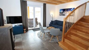 Ett modernt vardagsrum med ett träpanelat tak, en soffa, en tv och en trappa.