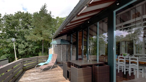 A wooden deck with outdoor furniture, including a table and chairs, and a covered seating area with an umbrella. - Bungalow With View Near Coo (Stavelot)