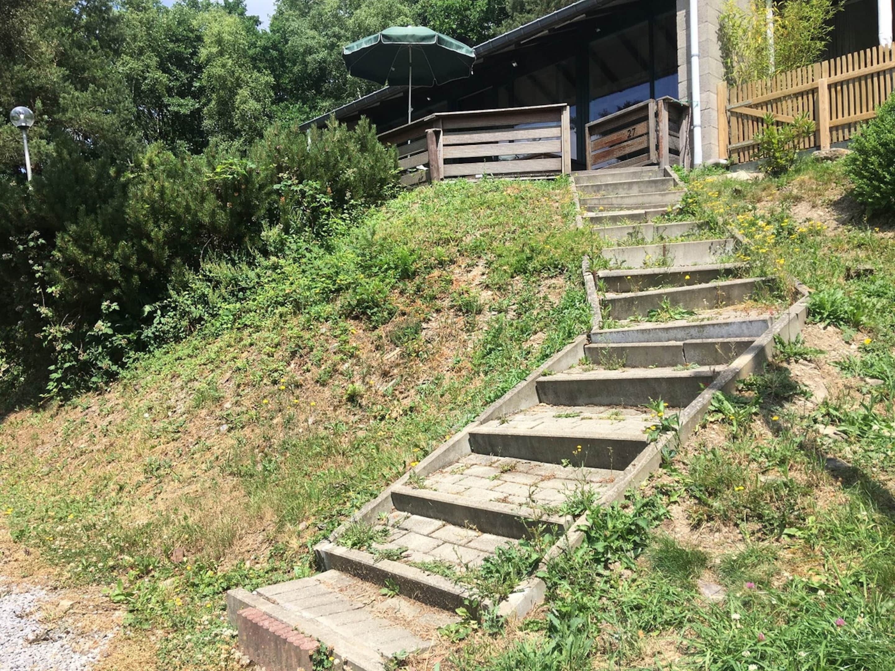 A set of concrete steps leading up to a wooden structure with a green umbrella.