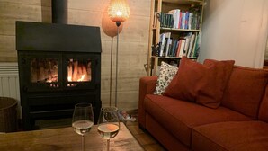A cozy room with a wood-burning stove, a bookshelf, a red sofa, and two glasses of wine on a wooden table. - Bungalow With View Near Coo (Stavelot)